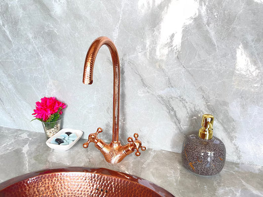 Handmade Copper Wall Mount Faucet with hammered finish and double handles installed above a copper sink in a bathroom setting.