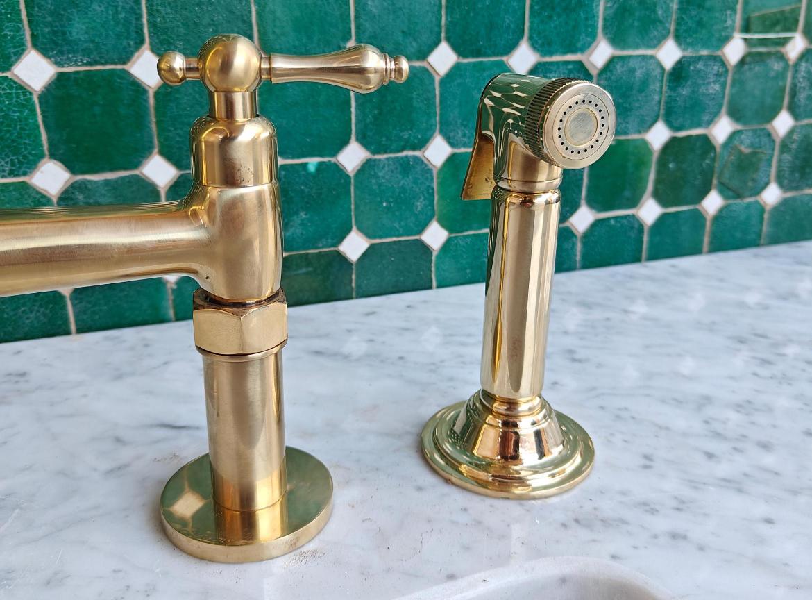 Bridge kitchen faucet with side sprayer in unlacquered brass finish, featuring durable metal construction for modern kitchen use.