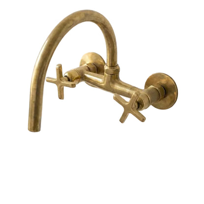 Unlacquered Brass Wall-Mount Bridge Faucet with Cross Handles installed above a white sink on a textured white wall.